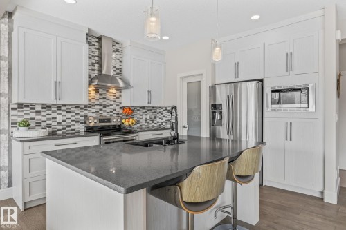 The kitchen features an island with a dark countertop and seating, white cabinetry, and stainless steel appliances - 3864 Robins Crescent, Edmonton, AB - Indoor Photo Showing Kitchen With Upgraded Kitchen