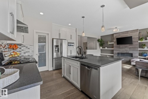 The property features a kitchen with white cabinetry, stainless steel appliances, a dark countertop, and a kitchen island with pendant lighting - 3864 Robins Crescent, Edmonton, AB - Indoor Photo Showing Kitchen With Fireplace With Double Sink With Upgraded Kitchen