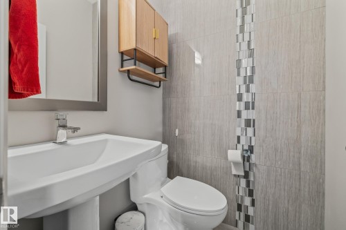 Powder room featuring a sleek white sink with a modern faucet, a wooden wall-mounted cabinet with open shelving, and stylish gray wall tiles with a decorative mosaic accent - 3864 Robins Crescent, Edmonton, AB - Indoor Photo Showing Bathroom