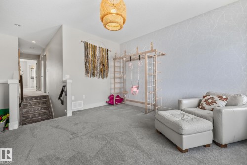 This spacious room features gray carpeting, light gray walls with a decorative accent wall, and a staircase with gray carpeted steps - 3864 Robins Crescent, Edmonton, AB - Indoor Photo Showing Other Room