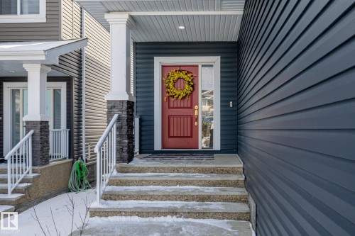 The property features a bold red entry door with a sidelight, set under a covered porch with white columns and stone accents - 3864 Robins Crescent, Edmonton, AB - Outdoor