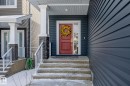 The property features a bold red entry door with a sidelight, set under a covered porch with white columns and stone accents - 3864 Robins Crescent, Edmonton, AB  - Outdoor 