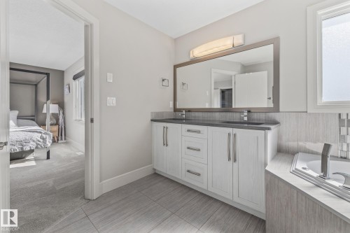Bathroom featuring a double vanity with white cabinetry, a large mirror, and a bathtub with tile surround - 3864 Robins Crescent, Edmonton, AB - Indoor Photo Showing Bathroom