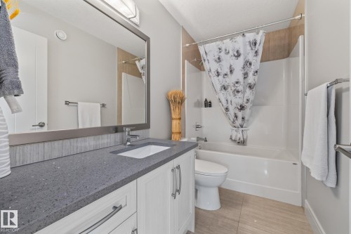 The bathroom features a vanity with a dark countertop and white cabinetry, a large mirror, and a bathtub with a shower and a floral shower curtain - 3864 Robins Crescent, Edmonton, AB - Indoor Photo Showing Bathroom