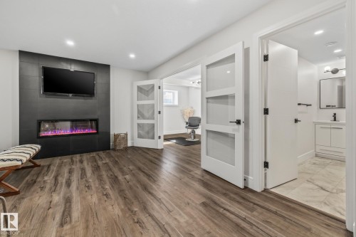 The property features durable wood-look flooring, a modern wall-mounted fireplace with a media niche, and recessed lighting - 3864 Robins Crescent, Edmonton, AB - Indoor With Fireplace