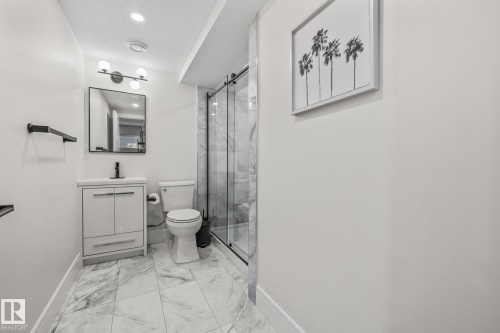 This bathroom features a contemporary vanity with a white countertop and dark-toned faucet, a glass-enclosed shower with marble-patterned walls, and a toilet - 3864 Robins Crescent, Edmonton, AB - Indoor Photo Showing Bathroom