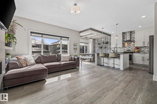 Open concept living space featuring wide plank flooring, a kitchen with white cabinetry, a large island with seating, and stainless steel appliances - 3864 Robins Crescent, Edmonton, AB - Indoor