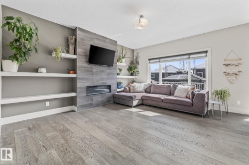 Living area featuring light hardwood floors, built-in shelving, and a modern fireplace with a tiled surround - 3864 Robins Crescent, Edmonton, AB - Indoor Photo Showing Living Room With Fireplace