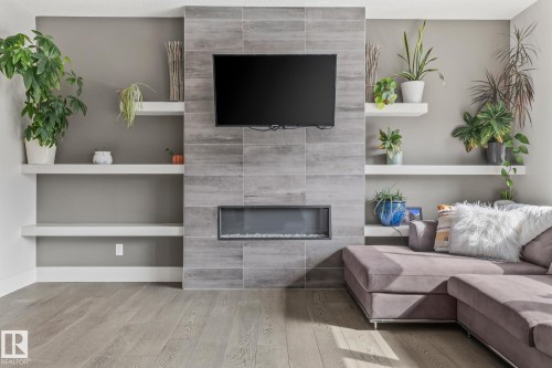 Living space featuring a tiled fireplace with an integrated electric firebox, an entertainment area with a mounted television, and floating shelves - 3864 Robins Crescent, Edmonton, AB - Indoor Photo Showing Other Room With Fireplace