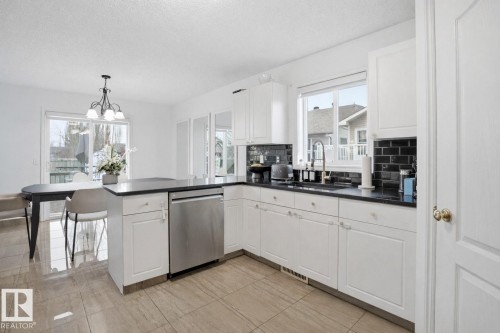 The kitchen features white cabinetry, dark countertops, a dark subway tile backsplash, and a stainless steel dishwasher - 4619 202 Street, Edmonton, AB - Indoor Photo Showing Kitchen