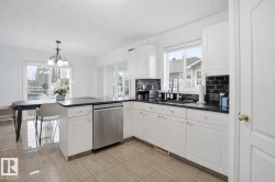 The kitchen features white cabinetry, dark countertops, a dark subway tile backsplash, and a stainless steel dishwasher - 