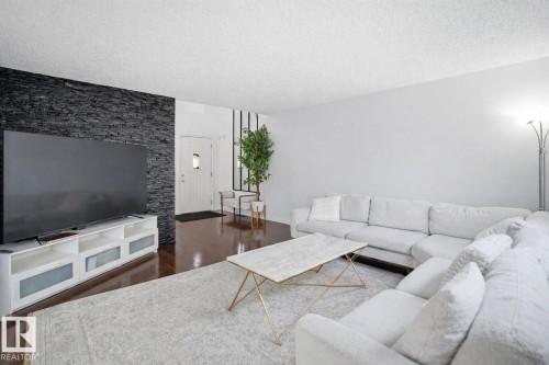The living area features polished hardwood floors, a white door with a window, and a wall with dark stacked stone - 4619 202 Street, Edmonton, AB - Indoor Photo Showing Living Room