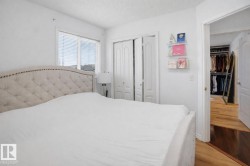 This bedroom features a window with blinds, bi-fold closet doors, and hardwood flooring visible through the doorway - 