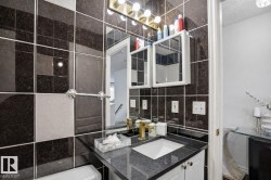 Bathroom featuring dark tiled walls with light accent tiles, a vanity with a dark speckled countertop, and a gold-toned faucet - 