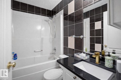 Bathroom featuring a vanity with a dark countertop and a white sink, a modern gold-toned faucet, and a shower/tub combination with a white surround - 4619 202 Street, Edmonton, AB - Indoor Photo Showing Bathroom