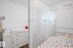 This room features white walls, a window with blinds, and white sheer curtains - 
