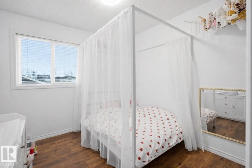 The room features warm-toned hardwood flooring and a window with blinds providing natural light - 4619 202 Street, Edmonton, AB - Indoor Photo Showing Bedroom