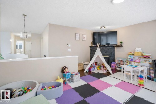 The property features a spacious room with a dark stone fireplace, a large television mounted above the fireplace, and ceiling lighting - 4619 202 Street, Edmonton, AB - Indoor Photo Showing Other Room