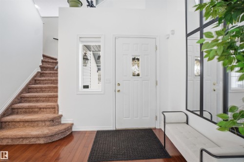 Welcoming entryway featuring hardwood flooring, a white front door with decorative glass, and a carpeted staircase - 4619 202 Street, Edmonton, AB - Indoor Photo Showing Other Room