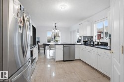 The kitchen features white cabinetry, dark countertops, stainless steel appliances, and a tile floor - 
