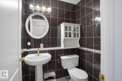 The bathroom features dark tiled walls, a white pedestal sink with a brass-toned faucet, and a wall-mounted mirror with a white frame - 