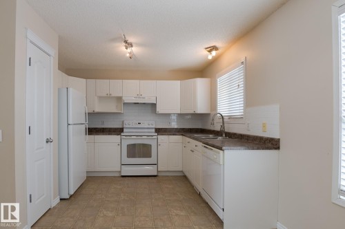The kitchen features white cabinetry, a white refrigerator, and a white oven with a matching range hood - 58 Birchmont Drive, Leduc, AB - Indoor Photo Showing Kitchen