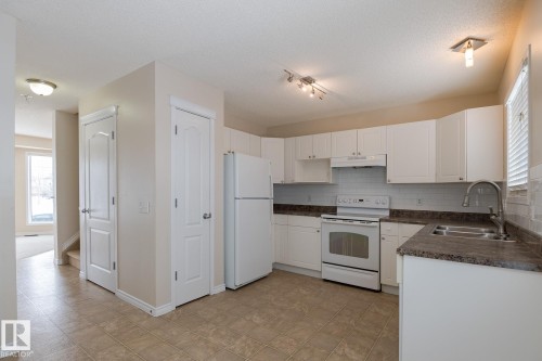 The kitchen features white cabinetry, a white refrigerator, and a white oven with a stovetop - 58 Birchmont Drive, Leduc, AB - Indoor Photo Showing Kitchen With Double Sink
