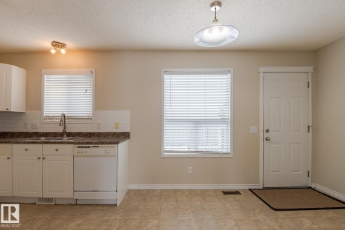The kitchen features white cabinetry, a double basin sink with a chrome faucet, and a white dishwasher - 58 Birchmont Drive, Leduc, AB - Indoor