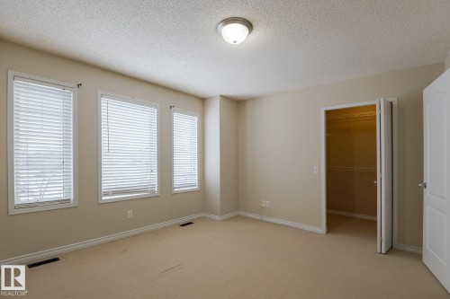Spacious room featuring three windows with blinds, a ceiling-mounted light fixture, and a built-in closet with shelving and hanging rods - 58 Birchmont Drive, Leduc, AB - Indoor