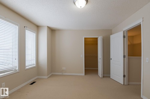 This room features two windows with blinds, a ceiling-mounted light fixture, and two open doorways revealing interior closet spaces - 58 Birchmont Drive, Leduc, AB - Indoor Photo Showing Other Room