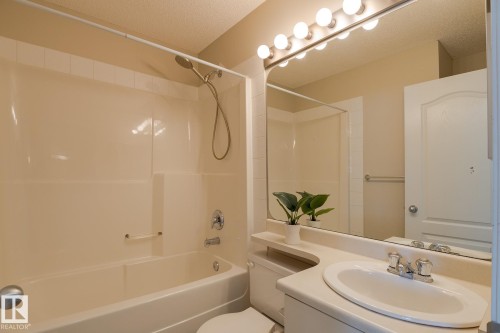 Bathroom featuring a full vanity with a built-in sink, a large mirror with overhead lighting, and a bathtub with an integrated shower head - 58 Birchmont Drive, Leduc, AB - Indoor Photo Showing Bathroom