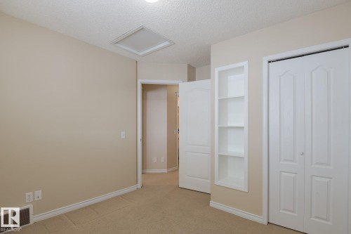 This room features neutral-toned walls, carpeted flooring, built-in shelving, and white bi-fold closet doors - 58 Birchmont Drive, Leduc, AB - Indoor