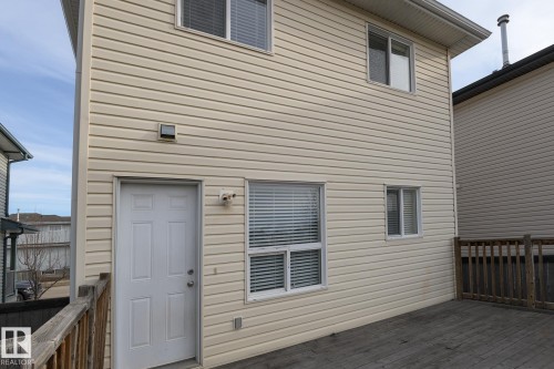 The property features light-colored horizontal siding, multiple windows with white frames, and a white exterior door - 58 Birchmont Drive, Leduc, AB - Outdoor With Exterior