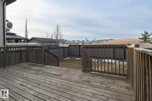The property features a spacious wooden deck with railings, offering views of the fenced backyard and surrounding neighborhood - 58 Birchmont Drive, Leduc, AB - Outdoor With Deck Patio Veranda