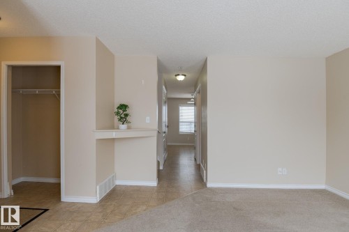 The property features neutral-toned walls, a combination of tiled and carpeted flooring, and a built-in shelving unit - 58 Birchmont Drive, Leduc, AB - Indoor Photo Showing Other Room