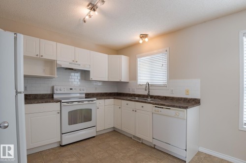 The kitchen features white cabinetry, a white tile backsplash, and a double basin stainless steel sink - 58 Birchmont Drive, Leduc, AB - Indoor Photo Showing Kitchen With Double Sink