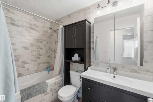 The bathroom features a bathtub with a shower, a vanity with an integrated sink, a wall-mounted mirror, and a storage cabinet - 4023 86 Street Nw, Edmonton, AB - Indoor Photo Showing Bathroom