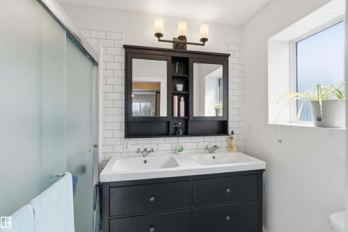 Bathroom featuring a double vanity with dark cabinetry, white subway tile backsplash, and a frosted glass shower door - 4023 86 Street Nw, Edmonton, AB - Indoor Photo Showing Bathroom
