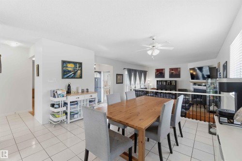 The property features an open-concept living space with white tiled flooring, a ceiling fan, and a view into a living area with a fireplace - 4023 86 Street Nw, Edmonton, AB - Indoor Photo Showing Dining Room