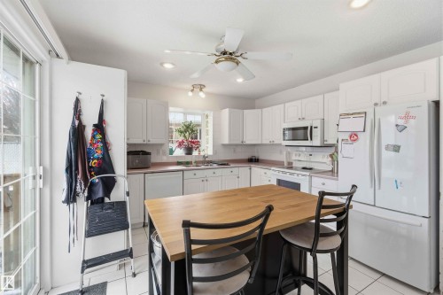 The kitchen features white cabinetry, a kitchen island with a wooden countertop, and a white refrigerator - 4023 86 Street Nw, Edmonton, AB - Indoor