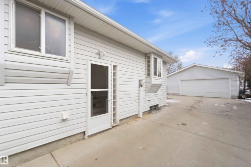 The property features light-colored siding, a visible window, and a door with a screen - 4023 86 Street Nw, Edmonton, AB - Outdoor With Exterior