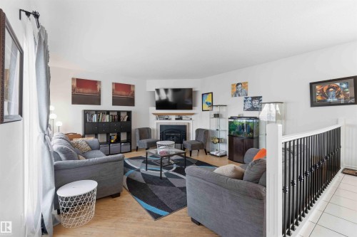 This living area features light-toned flooring, a corner fireplace with a white mantel, and a black and white staircase railing - 4023 86 Street Nw, Edmonton, AB - Indoor Photo Showing Living Room With Fireplace