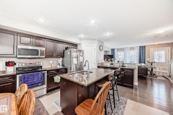 The kitchen features dark wood cabinetry, stainless steel appliances, granite countertops, and a central island with a sink and seating - 