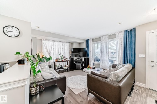This living space features hardwood flooring, light-colored walls, and large windows with both sheer and blue curtains - 138 655 Tamarack Road Nw, Edmonton, AB - Indoor Photo Showing Living Room