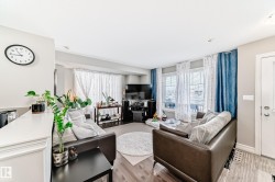 This living space features hardwood flooring, light-colored walls, and large windows with both sheer and blue curtains - 