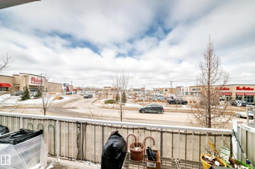 The property features a balcony with a white railing, offering views of a commercial area with various retail establishments and a parking lot - 138 655 Tamarack Road Nw, Edmonton, AB - Outdoor