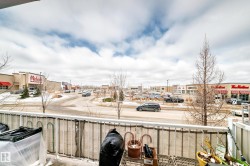 The property features a balcony with a white railing, offering views of a commercial area with various retail establishments and a parking lot - 