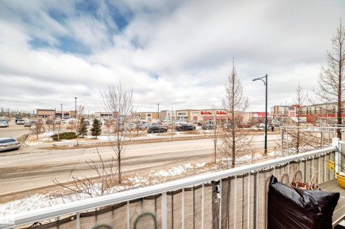 This property offers a private balcony with a white railing, providing views of the surrounding neighborhood with commercial buildings and a road - 138 655 Tamarack Road Nw, Edmonton, AB - Outdoor With View