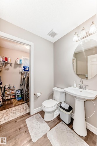 This bathroom features a pedestal sink with a round mirror, a toilet, and wood flooring - 138 655 Tamarack Road Nw, Edmonton, AB - Indoor