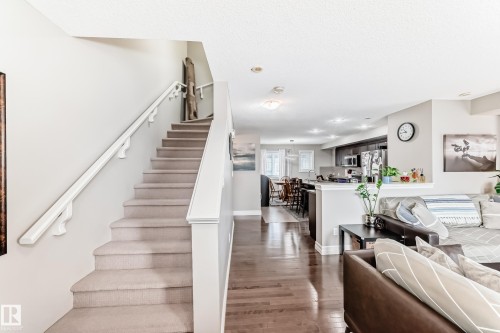 The property features carpeted stairs with a white handrail, leading to a bright open-concept living area with hardwood floors - 138 655 Tamarack Road Nw, Edmonton, AB - Indoor Photo Showing Other Room